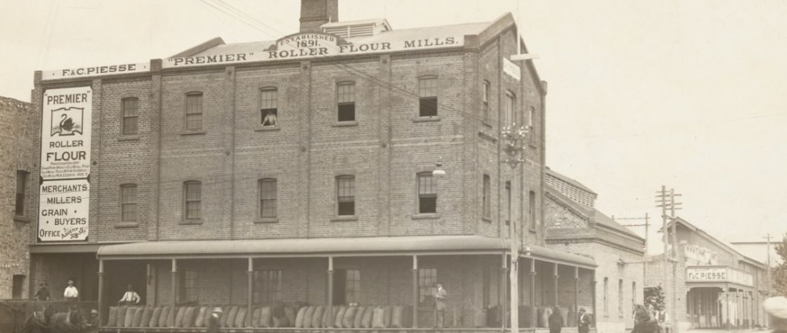 Image of the Premier Flour Mill circa 1912. Bags fille dwith grain line the verandah ready for collection.